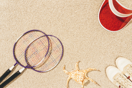 top view of arrangement of badminton equipment, cap and shoes on sandの写真素材