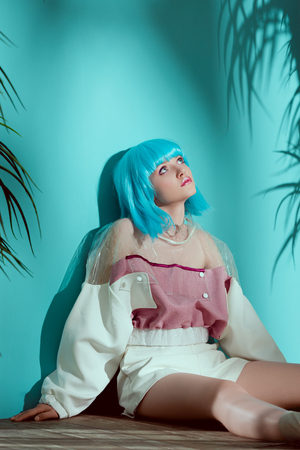 fashionable girl in blue wig sitting on floor and looking up