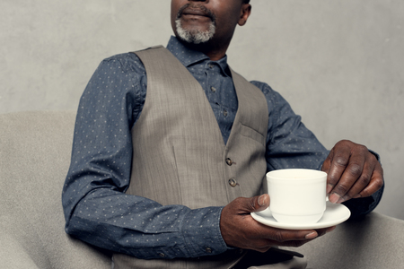 cropped view of stylish african american man in waistcoat holding cup of coffeeの写真素材