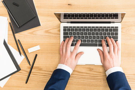 cropped shot of businessman working on laptop at workplace with notebooksの写真素材