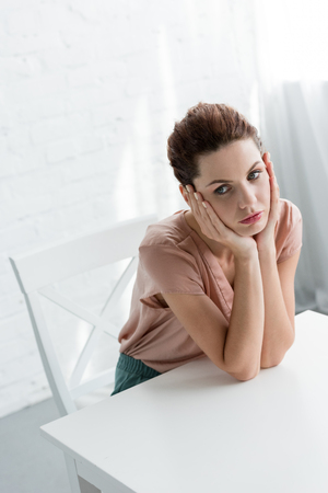 depressed young woman sitting at table in front of white brick wallの写真素材