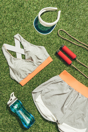 top view of arranged sportswear, water bottle, jump rope and cap on green grassの写真素材