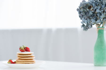 tasty pancakes with strawberries and flowers in vase on tableの写真素材