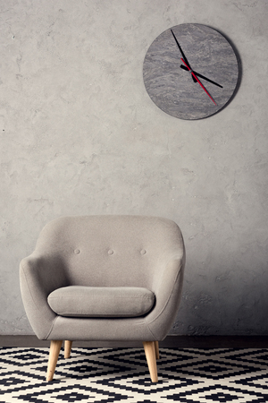 armchair, carpet and clock on wall in simple grey roomの写真素材