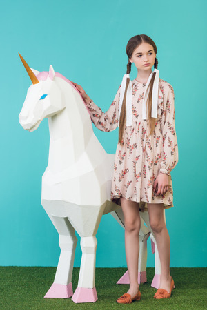 fashionable youth girl posing with big white unicorn on turquoiseの写真素材
