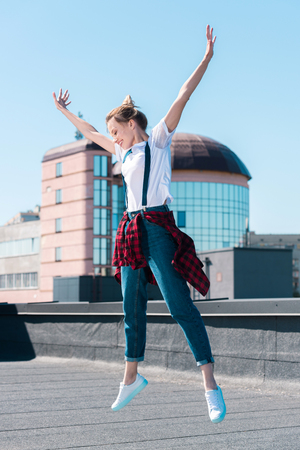 young smiling woman jumping with wide arms up at rooftopの写真素材