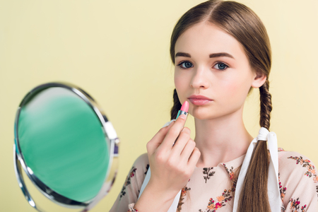 beautiful teen girl applying lipstick with mirror, isolated on yellowの写真素材