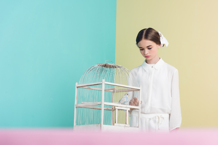 attractive fashionable girl with parrot in white cageの写真素材