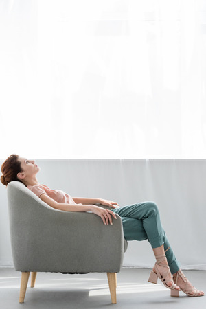attractive young woman relaxing on comfy armchair at homeの写真素材