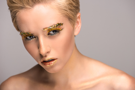 attractive irritated woman with golden glittering makeup isolated on greyの写真素材