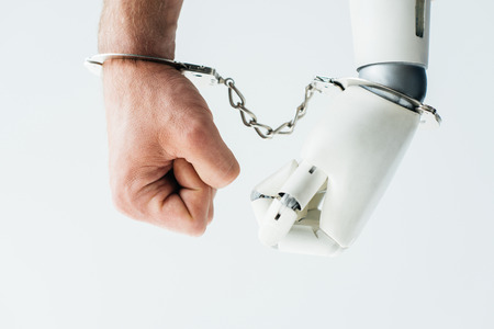close-up view of human hand and hand of robot in handcuffs isolated on whiteの写真素材
