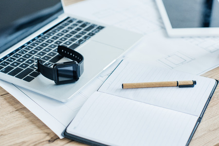 close-up view of smartwatch, laptop, digital tablet, blueprint and notebook at workplaceの写真素材