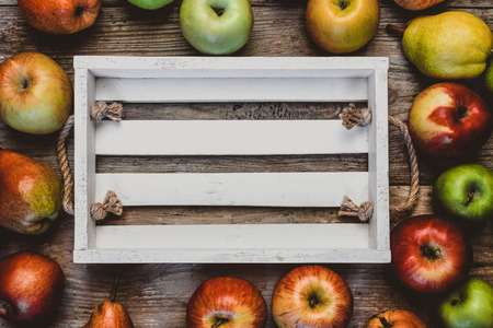 top view of empty wooden box surrounded by pears and apples on tableの写真素材