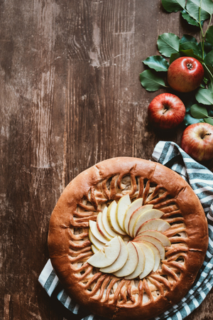 top view of arranged apple pie and fresh apples with green leaves on wooden surfaceの写真素材