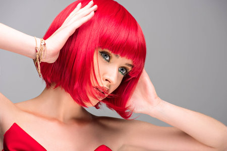 attractive woman with red hair and glitter on face touching head isolated on greyの写真素材