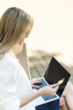 young blonde woman holding credit card and using laptopの写真素材