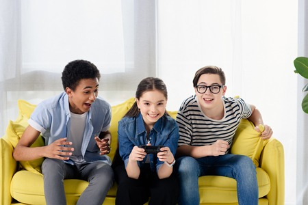 multicultural teen boys supporting friend playing video game at home