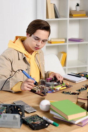 teen boy soldering computer circuit with soldering iron at home
