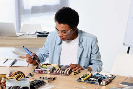 african american teenager soldering computer circuit with soldering iron at homeの写真素材