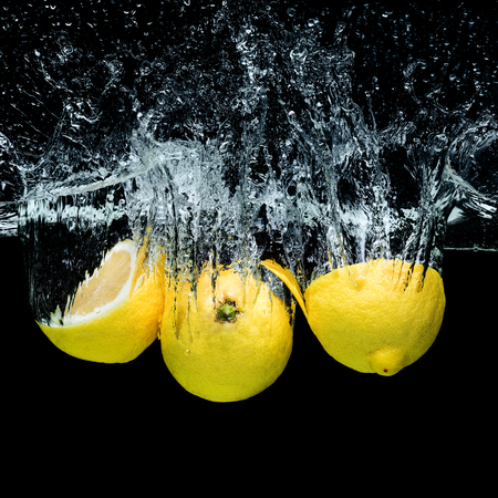 close up view of fresh lemons in water with splashes isolated on blackの写真素材