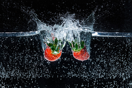 close up view of motion of ripe strawberries falling into water isolated on blackの写真素材