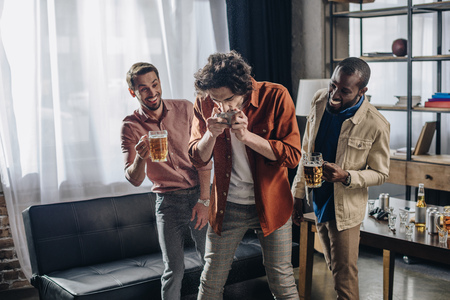 laughing male friends looking at man drinking beer from can