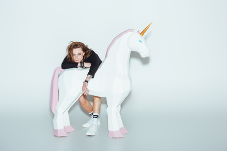 stylish man posing in black jacket with big white unicorn, on greyの写真素材