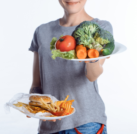 cropped shot of woman holding plates with vegetables and junk foodの写真素材