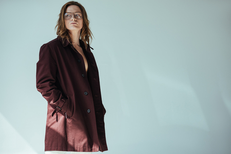stylish elegant man in glasses posing in trench coat, isolated on greyの写真素材