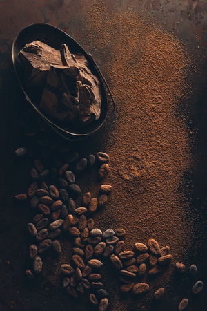 top view of delicious chocolate pieces, cocoa beans and powder on dark surfaceの写真素材