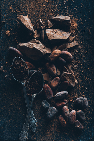 top view of vintage spoons, chocolate pieces and cocoa beans on dark surfaceの写真素材