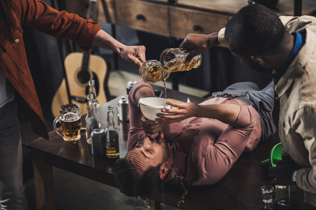 cropped shot of friends pouring beer in funnel and man drinking while lying on tableの写真素材