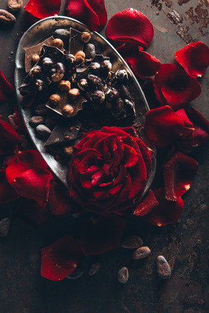 top view of beautiful red rose petals and gourmet chocolate with hazelnuts on dark surfaceの写真素材