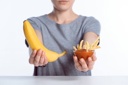 cropped shot of girl holding ripe banana and ketchup with french friesの写真素材