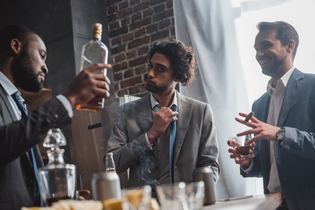 low angle view of young multiethnic businessmen smoking cigars and drinking whiskyの写真素材