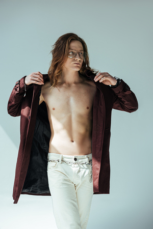 fashionable shirtless man posing in trench coat, on greyの写真素材