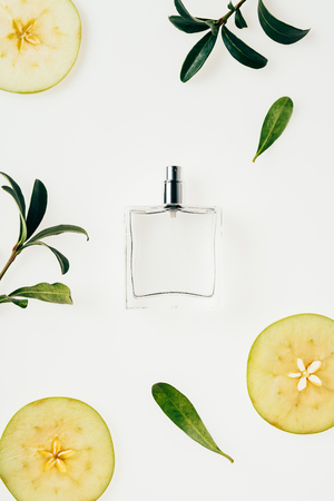 top view of glass bottle of perfume surrounded with green branches and apple slices on whiteの写真素材