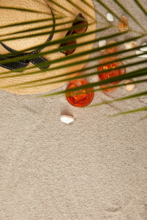 top view of arranged straw hat, sunglasses, cocktails, seashells on sand and palm leafの写真素材