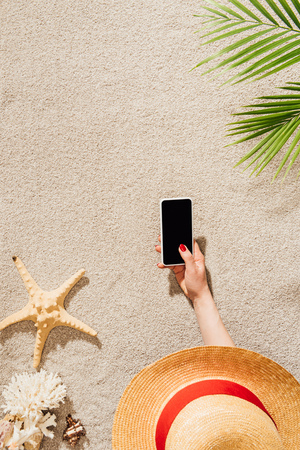 cropped shot of woman in hat using smartphone while lying on sandy beachの写真素材