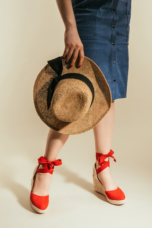 cropped shot of stylish woman in red platform sandals holding straw hat on beige backgroundの写真素材