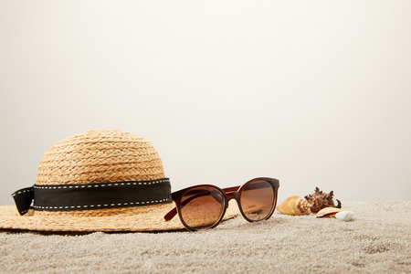 close up view of straw hat, sunglasses and seashells on sand on grey backdropの写真素材