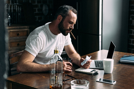 depressed young man smoking cigar and looking at crumpled photo of ex-girlfriendの写真素材