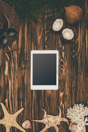 top view of digital tablet on wooden surface surrounded with various tropical travel attributesの写真素材