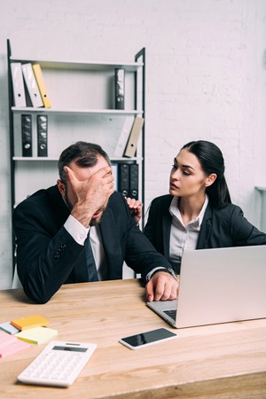 overworked businessman and business colleague at workplace with laptop in officeの写真素材