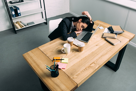 high angle view of overworked businesswoman sleeping at workplace with laptop and coffee to go in officeの写真素材