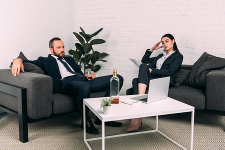 tired business colleagues at coffee table with laptop and alcohol in officeの写真素材