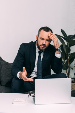 portrait of stressed businessman in suit looking at laptop on coffee table in officeの写真素材