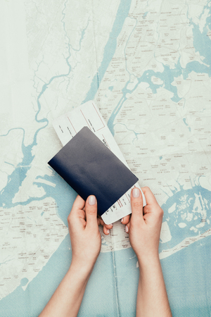 cropped shot of woman holding flight ticket and passport on travel mapの写真素材