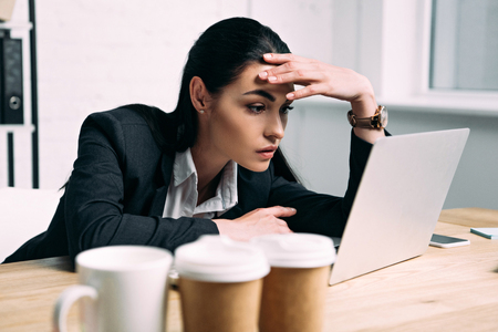 side view of tired businesswoman in suit working on laptop at workplace in officeの写真素材