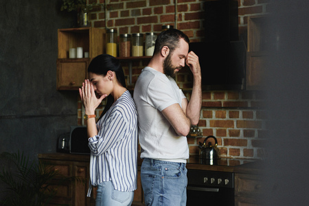 side view of young depressed couple standing back to back after quarrel at homeの写真素材